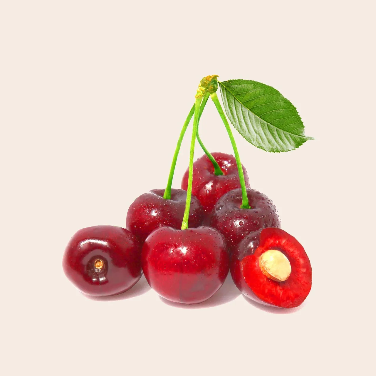 Kırmızı kirazlar ve ortadan kesilmiş bir kirazın içinde görünen çekirdek, açık renk zeminde.